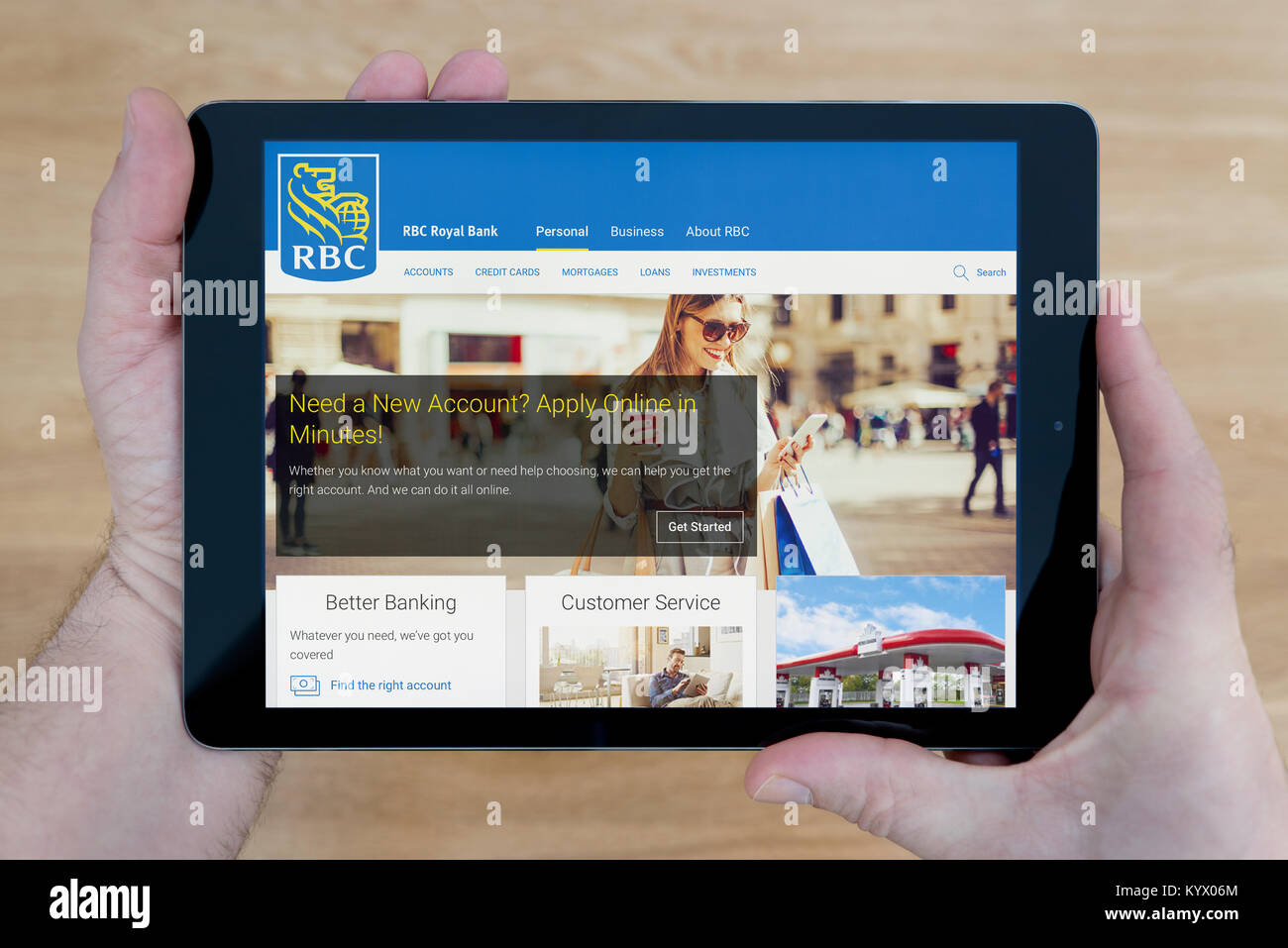 A man looks at the Royal Bank of Canada (RBC) website on his iPad tablet device, with a wooden table top background (Editorial use only) Stock Photo