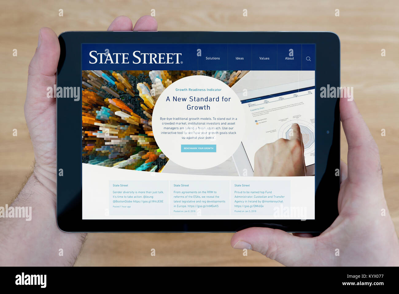 A man looks at the State Street Corporation website on his iPad tablet device, with a wooden table top background (Editorial use only) Stock Photo