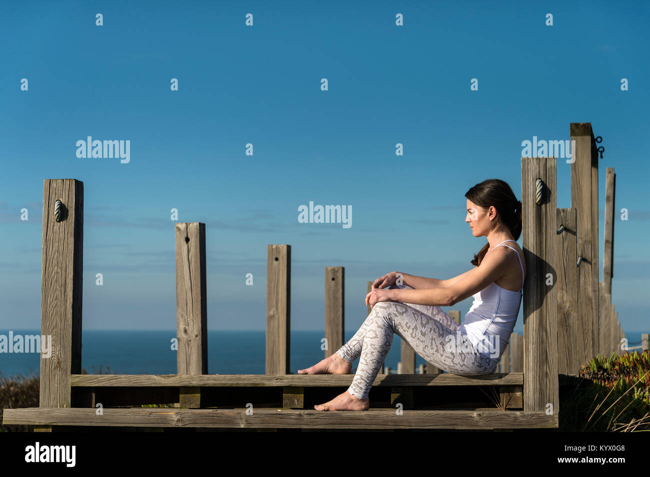woman sitting on wooden steps by the sea, thinking and relaxing in the sun. Stock Photo