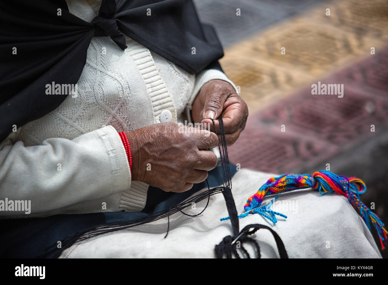 Otavalo, Ecuador - December 30, 2017: closeup of the hands an indigenous woman working on an artisan knotted souvenir in the local market Stock Photo