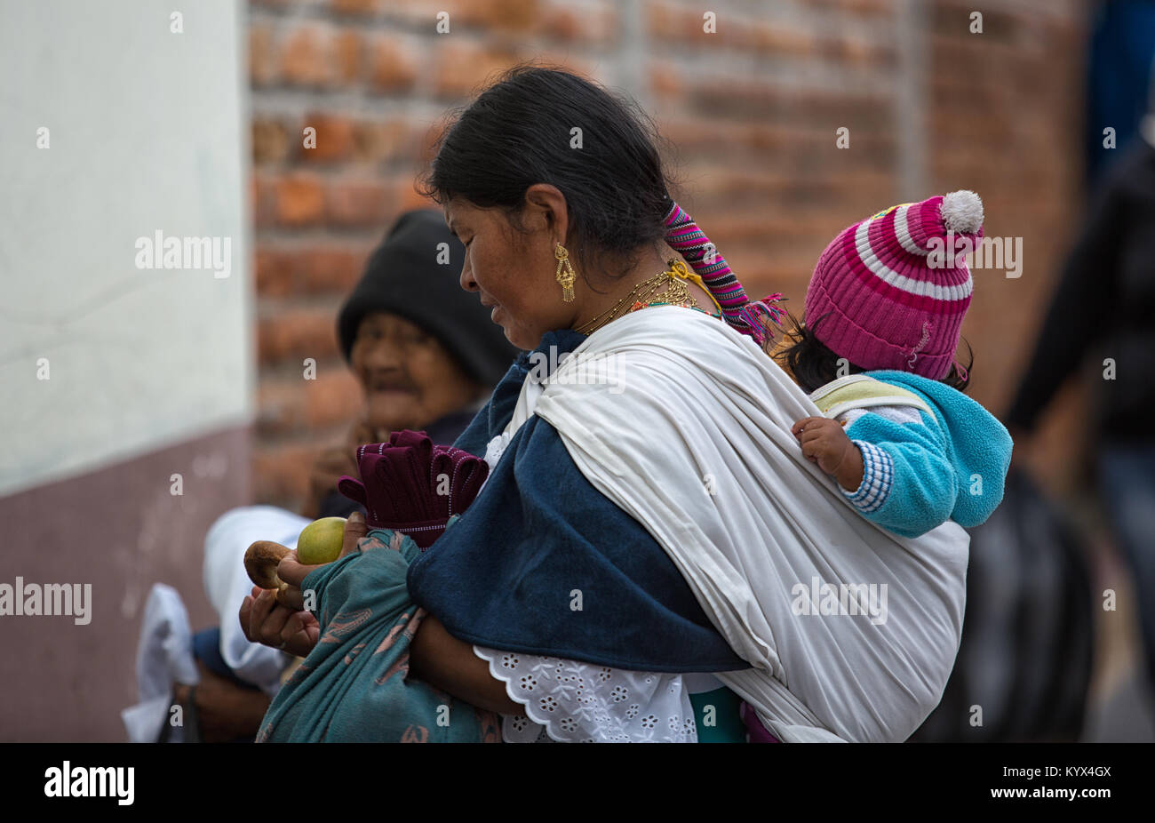 Otavalo, Ecuador - December 30, 2017: indigenous quechua woman carrying child on her back  in the local market Stock Photo