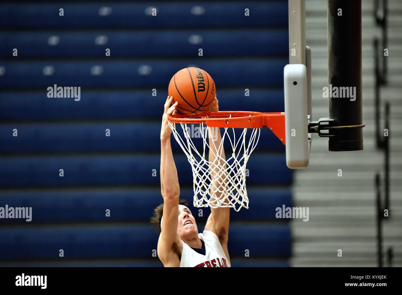 Forward hanging at the rim while slamming home two points during a high school game. USA. Stock Photo