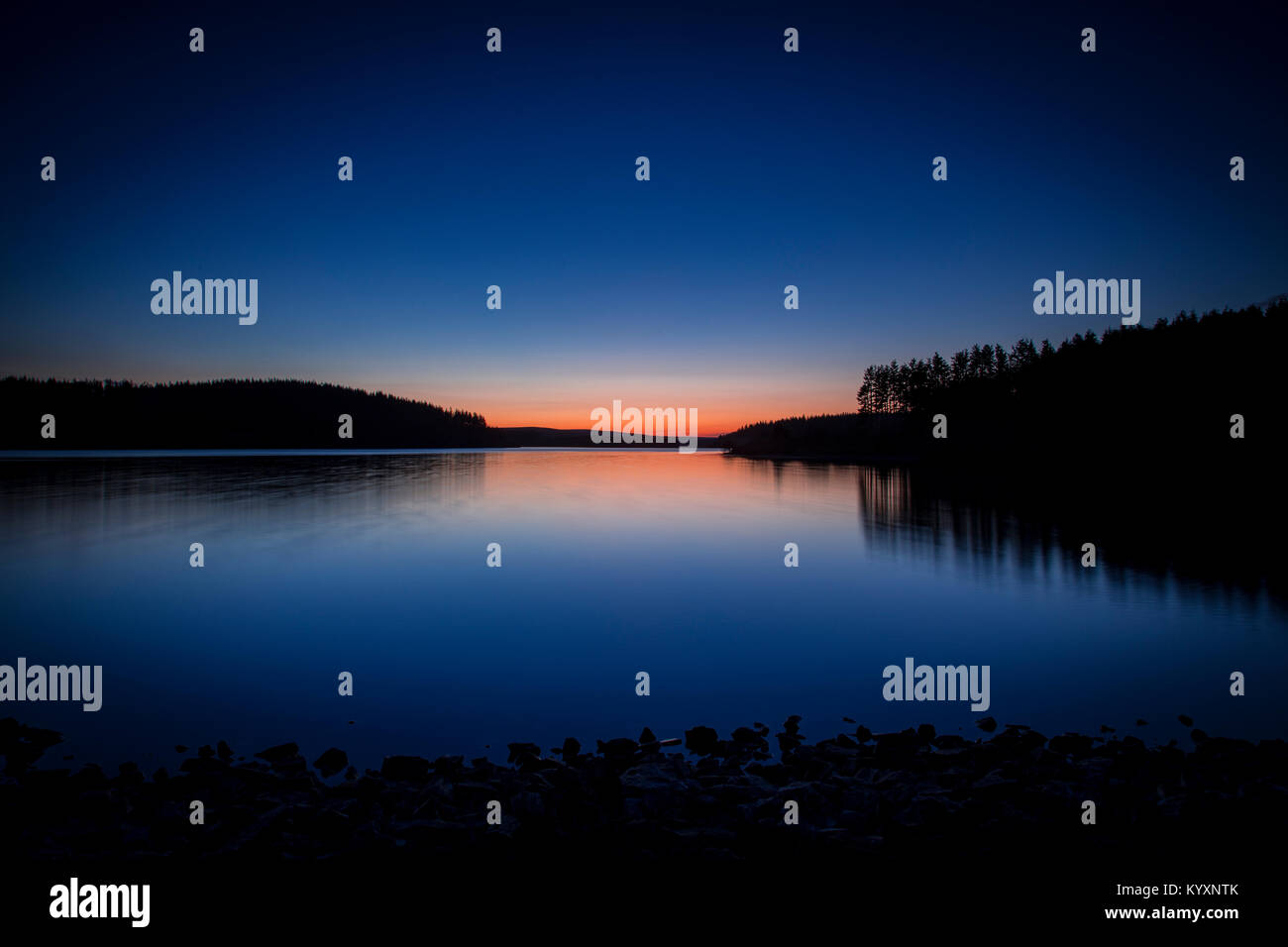 The colours of twilight reflecting in the calm, tree lined waters of Alwen Reservoir, Wales Stock Photo