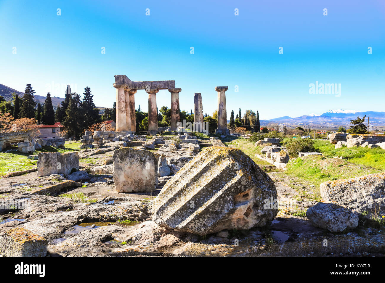 Broken columns in front of the remaining columns of the Temple of Apollo in ancient Corinth on the Peloponnese peninsula in Greece - snow covered moun Stock Photo