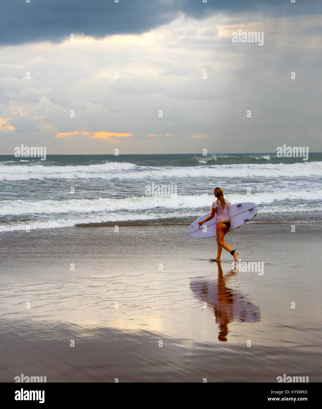 Woman surfer walking on the beach with surfboard at sunset. Bali island Stock Photo