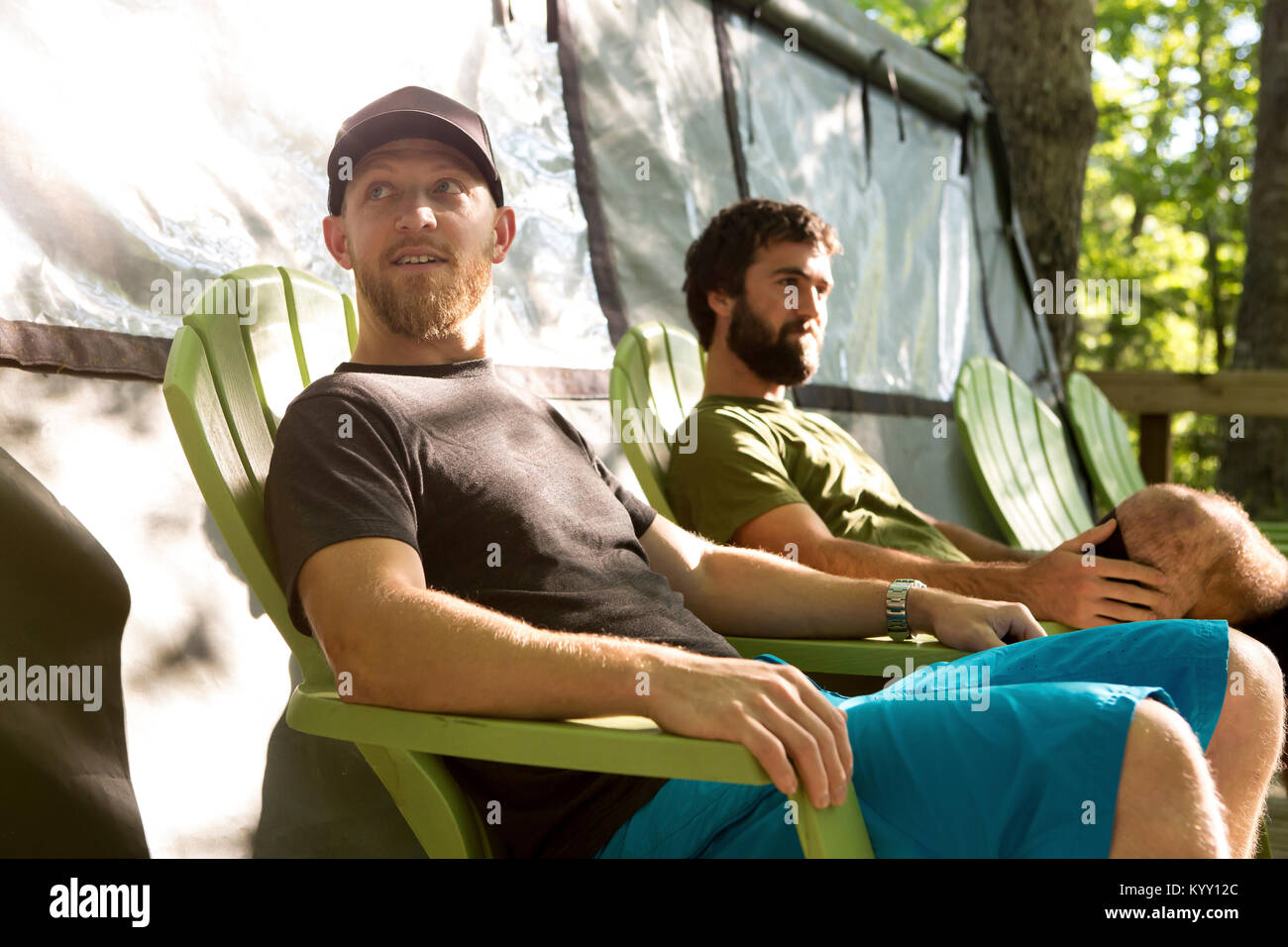 Friends sitting on chairs while relaxing by tent at campsite in forest ...