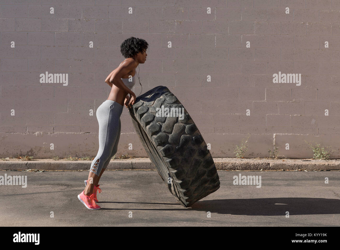 Full length of woman lifting tire truck while exercising against wall Stock Photo