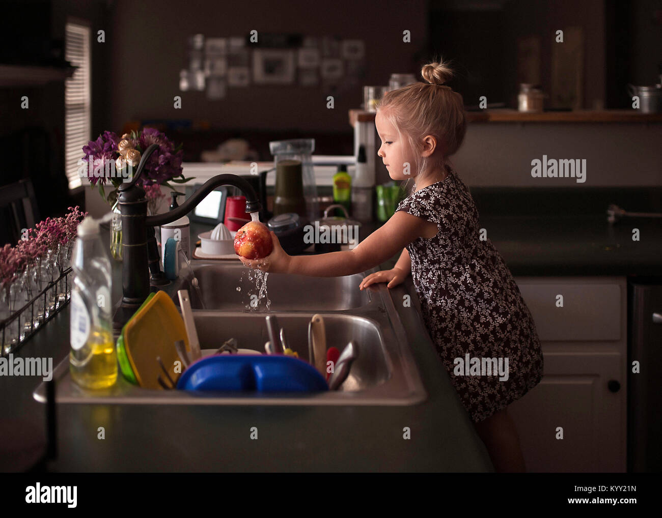 Side view of girl washing apple at kitchen sink Stock Photo