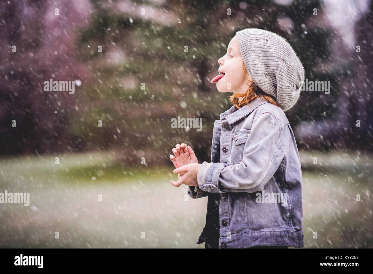 Side view of girl sticking out tongue while standing at park during snowfall Stock Photo
