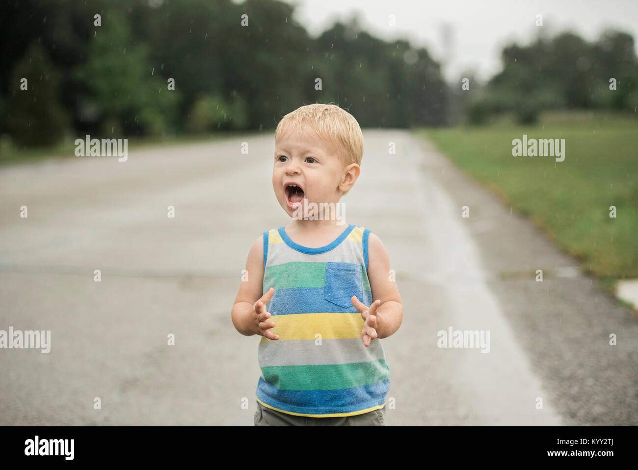 Cute boy shouting while looking away during rainfall on road Stock Photo