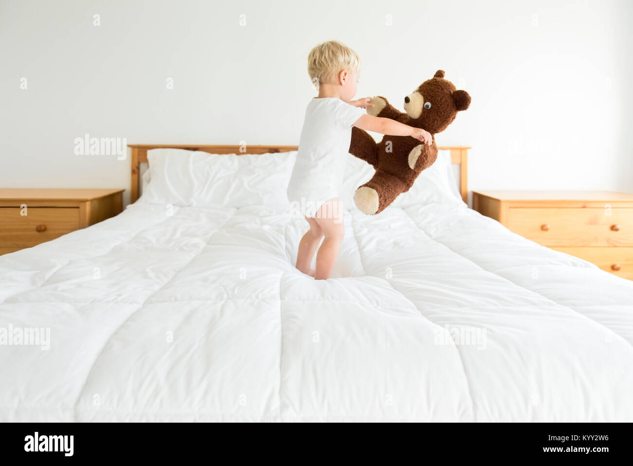 Cute boy playing with teddy bear while standing on bed Stock Photo - Alamy