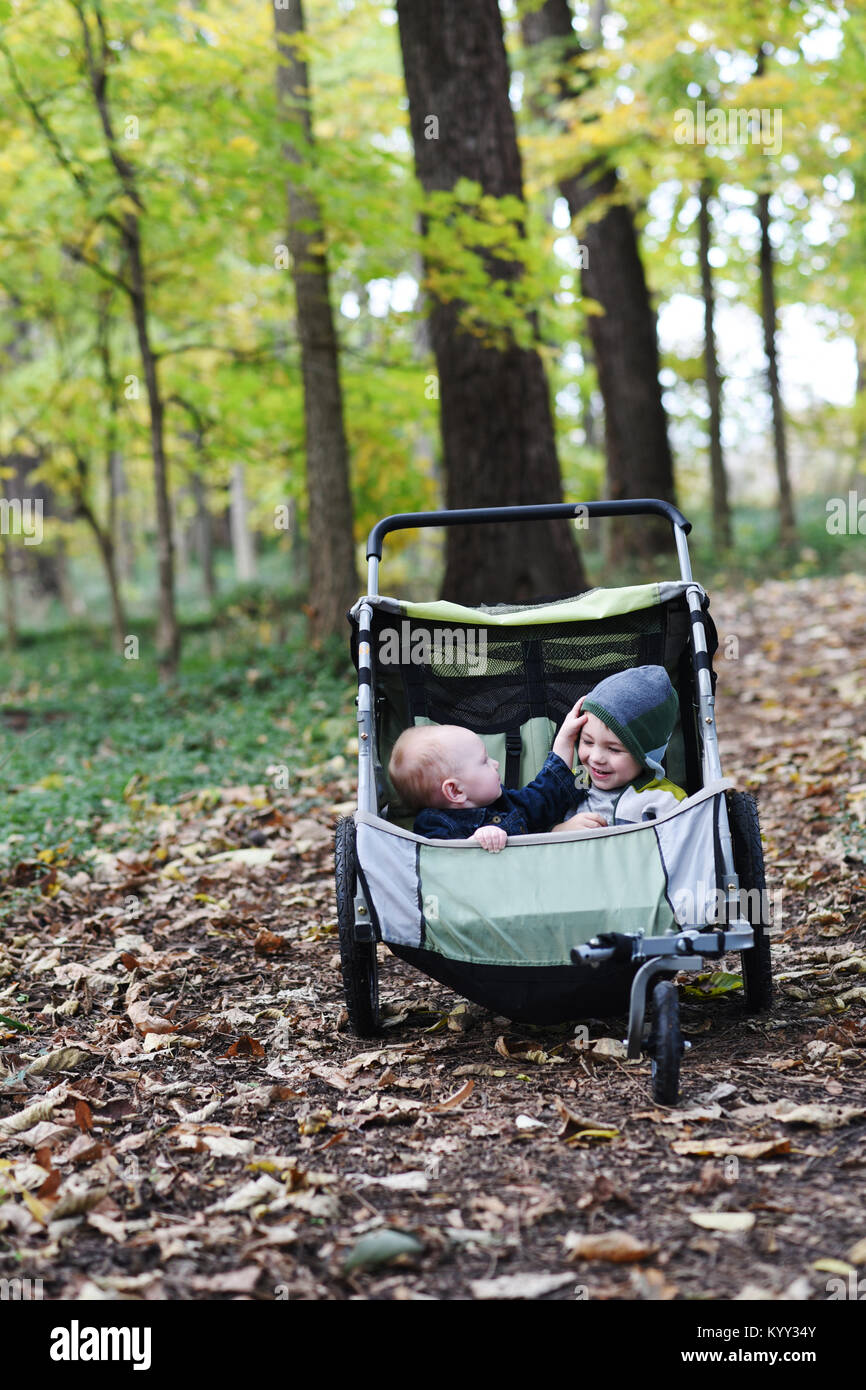 Toddler playing with brother sitting in baby stroller at park during autumn Stock Photo