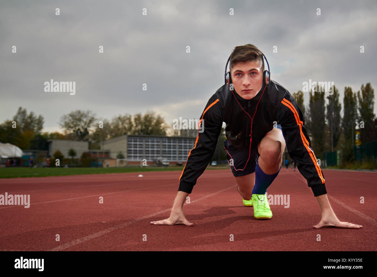 Full length of male athlete listening music while taking position at running track Stock Photo