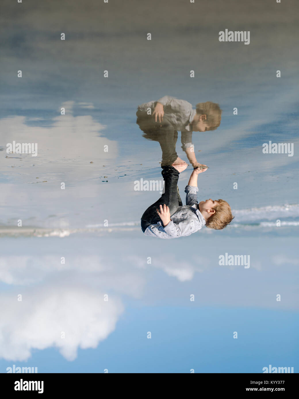Upside down image of boy playing on shore at beach against cloudy sky Stock Photo
