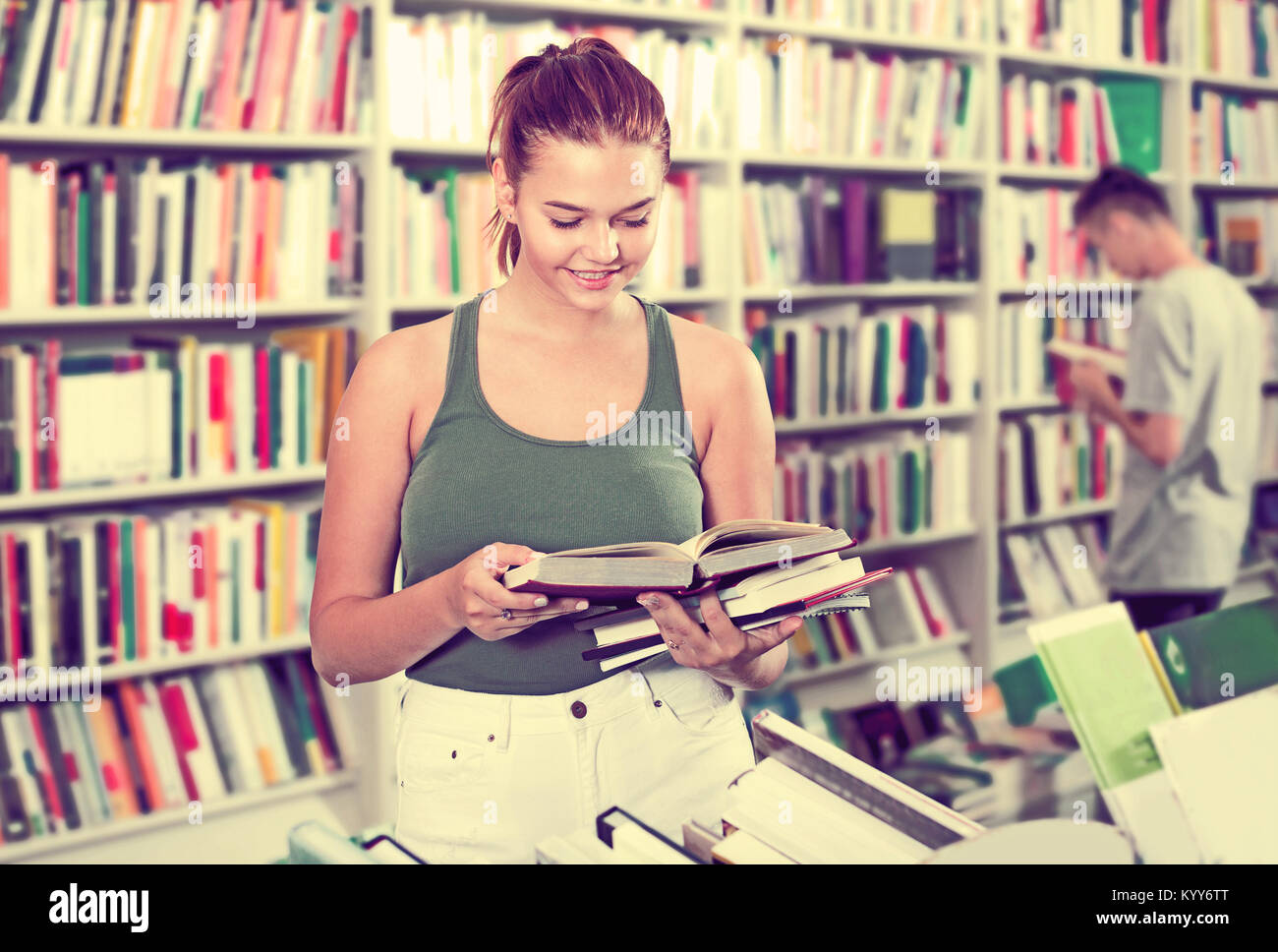 Happy teenager girl holding open book in hands and looking at it in ...