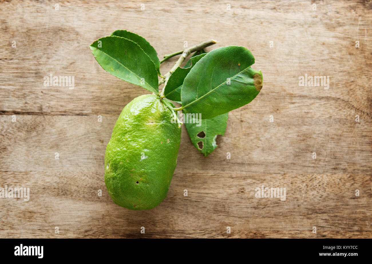 Top view fresh organic lemon with leaves on wooden table background, imperfect insect bites, pesticide free. Stock Photo