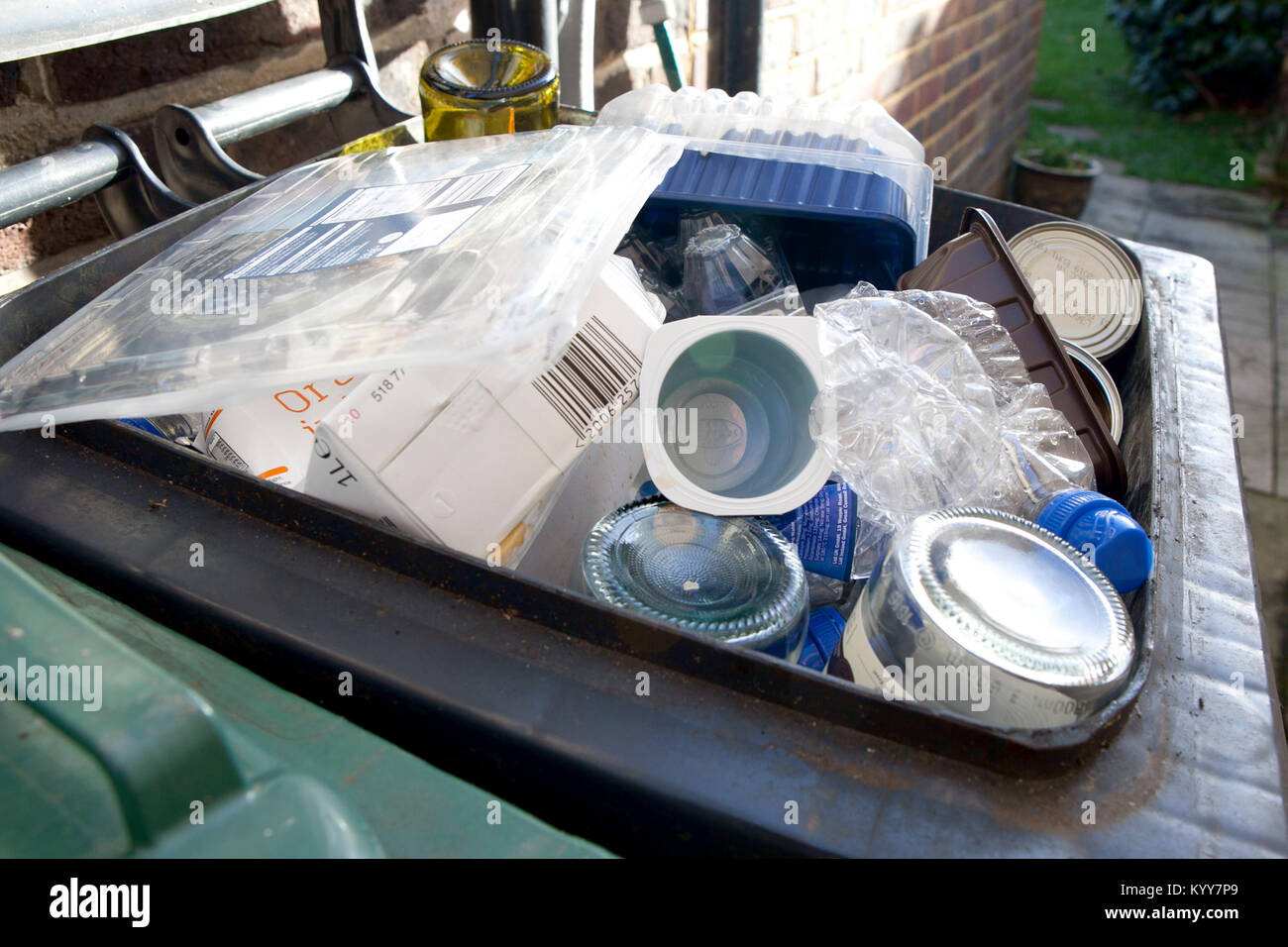 Wheelie bin full of domestic recycling waste, glass bottles, tin cans