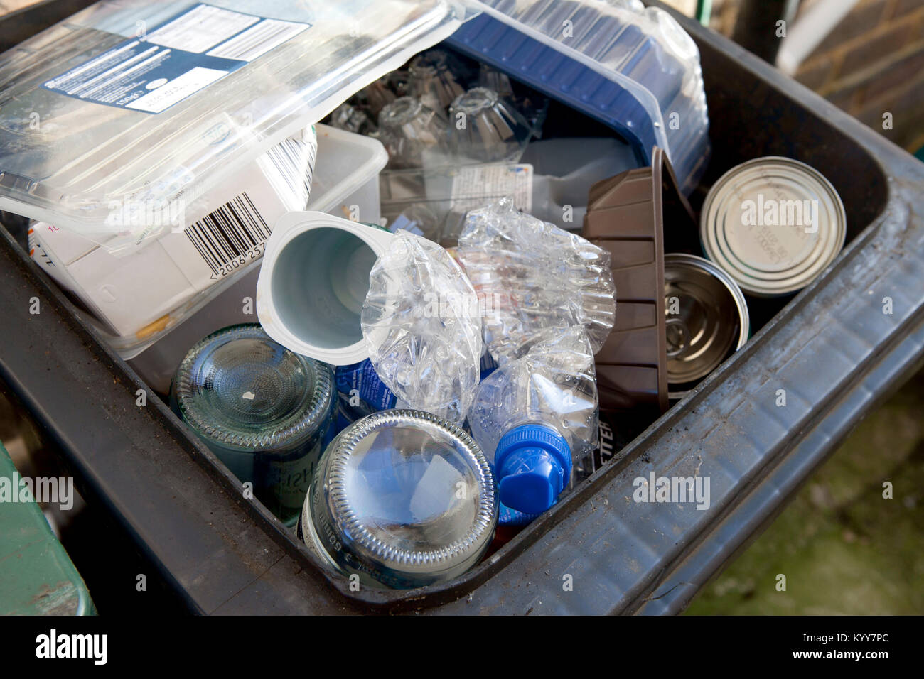 Wheelie bin full of domestic recycling waste, glass bottles, tin cans and plastic bottles, plastic waste, Recycling. Stock Photo