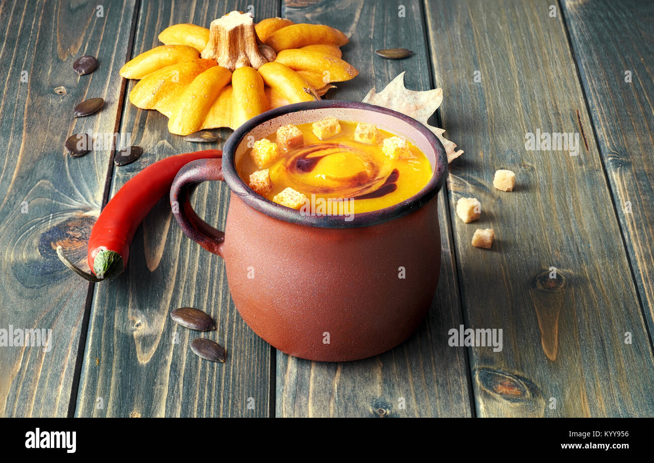 Spicy pumpkin soup in old enamel mug on rustic wooden table. The soup is served with croutons and pumpkin oil Stock Photo