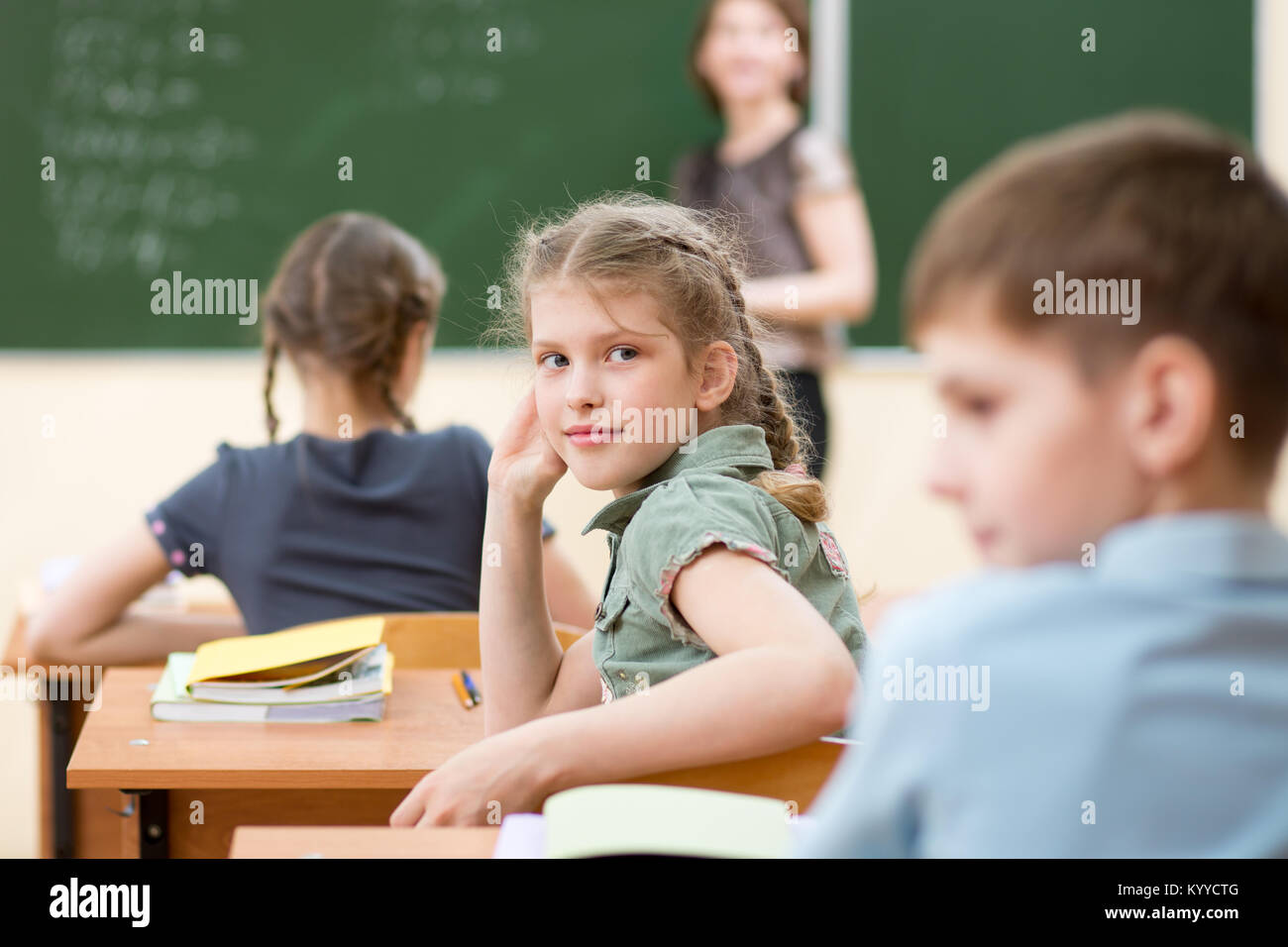 Happy schoolchildren sitting at desk in classroom, teacher at chalkboard Stock Photo