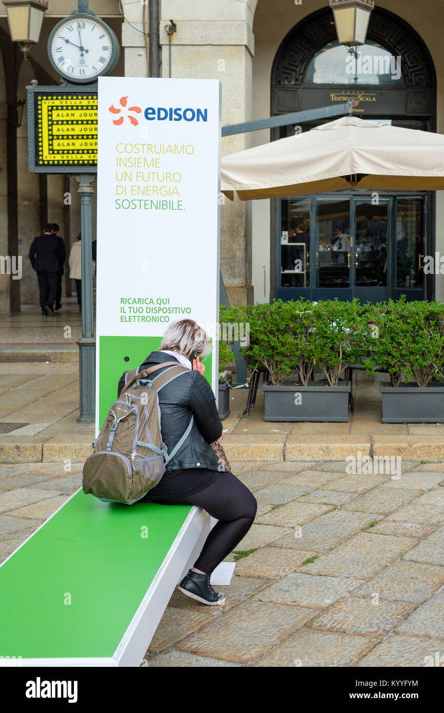 Woman using a mobile/cell phone at a Edison charging station, near La Scala theatre, Milan, Italy Stock Photo