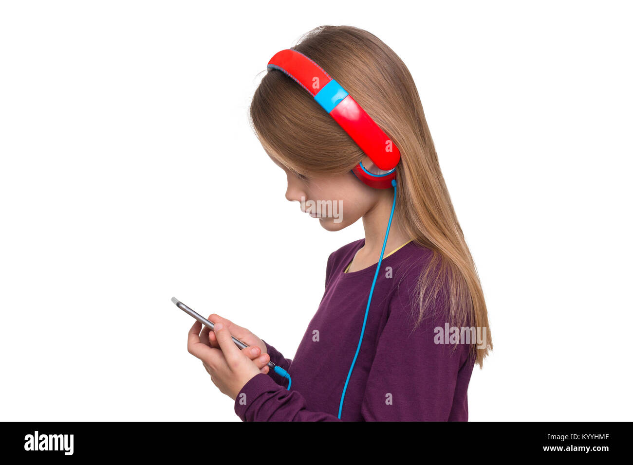 A 9 year old girl is wearing headphones and looking at a smartphone