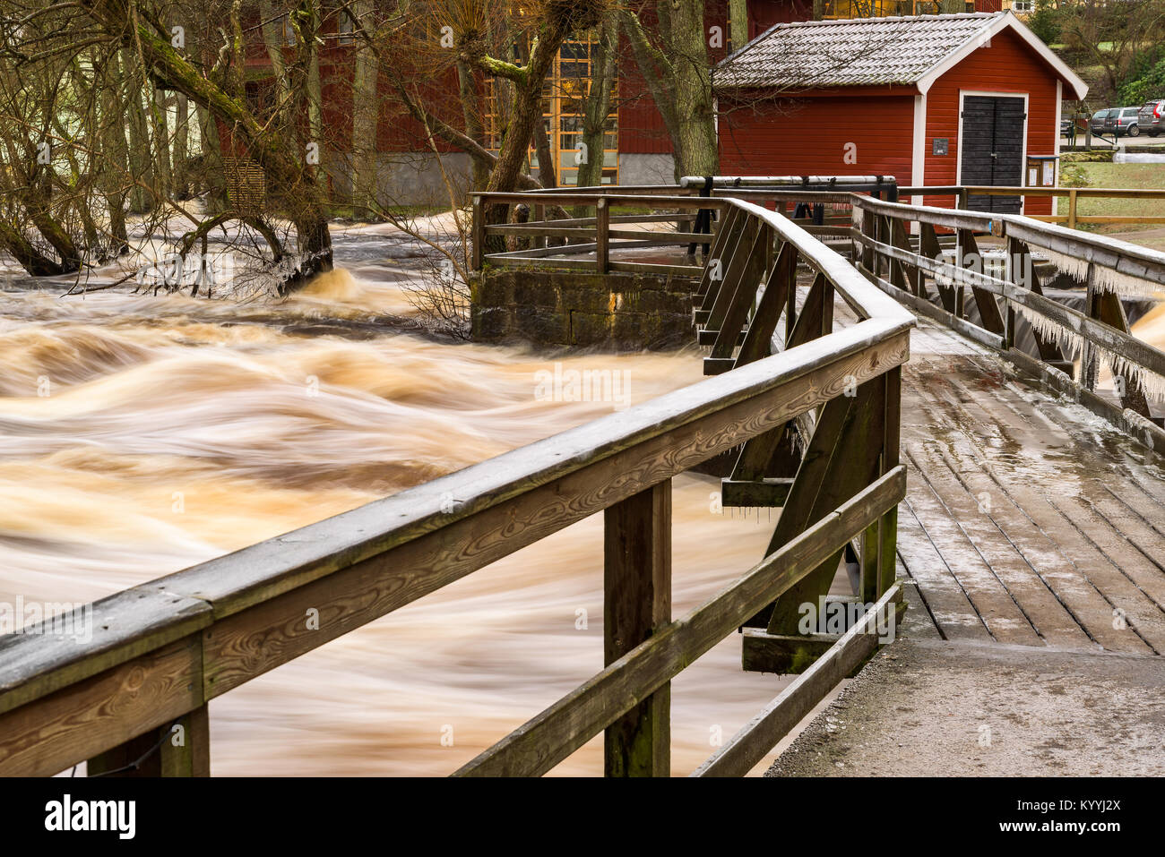 Morrum, Sweden - January 8, 2018: Documentary of everyday life and environment. Frozen bridge over raging river during flooding event. Buildings in th Stock Photo