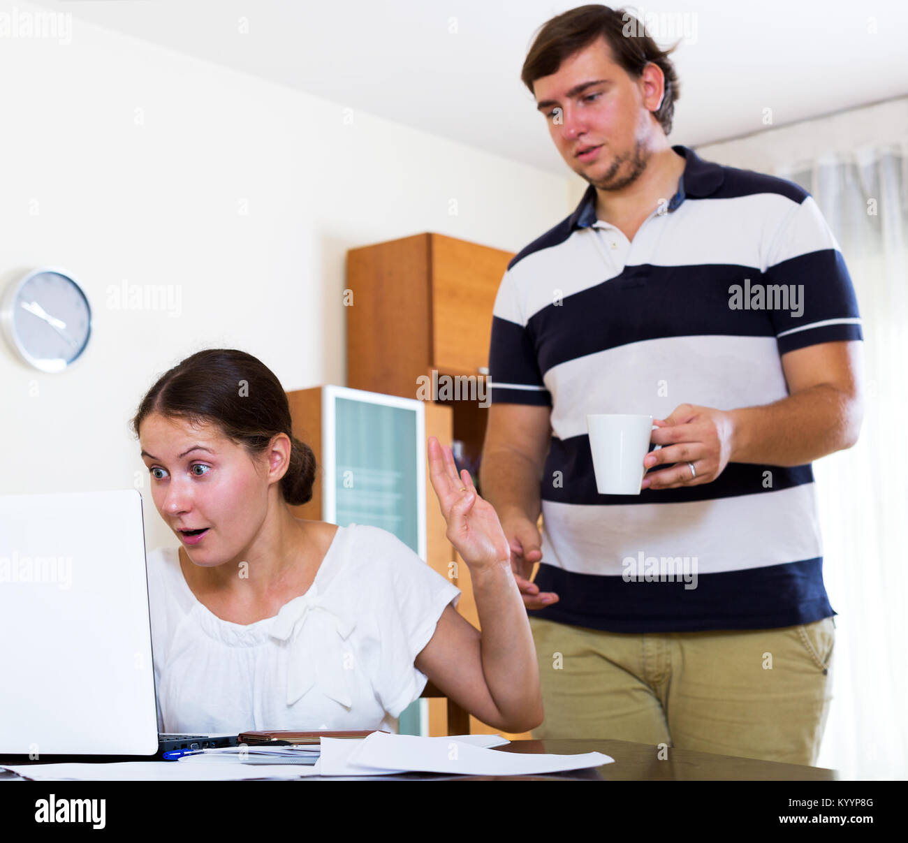 Portrait of young female working online and ignoring unhappy husband. Focus on the woman Stock Photo