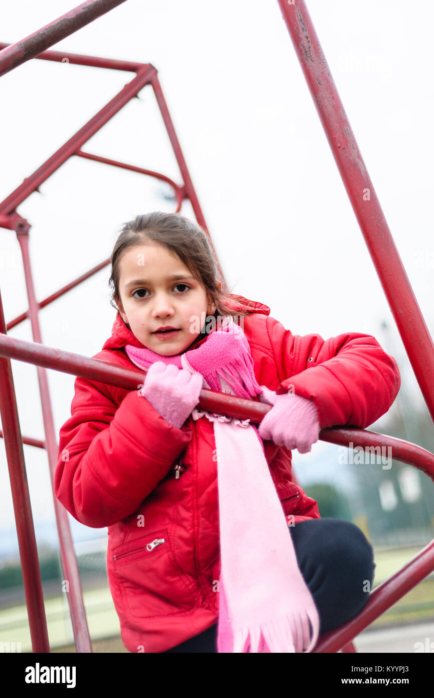 little girl climbs on iron frame of a basketball hoop in an outdoor basketball court Stock Photo