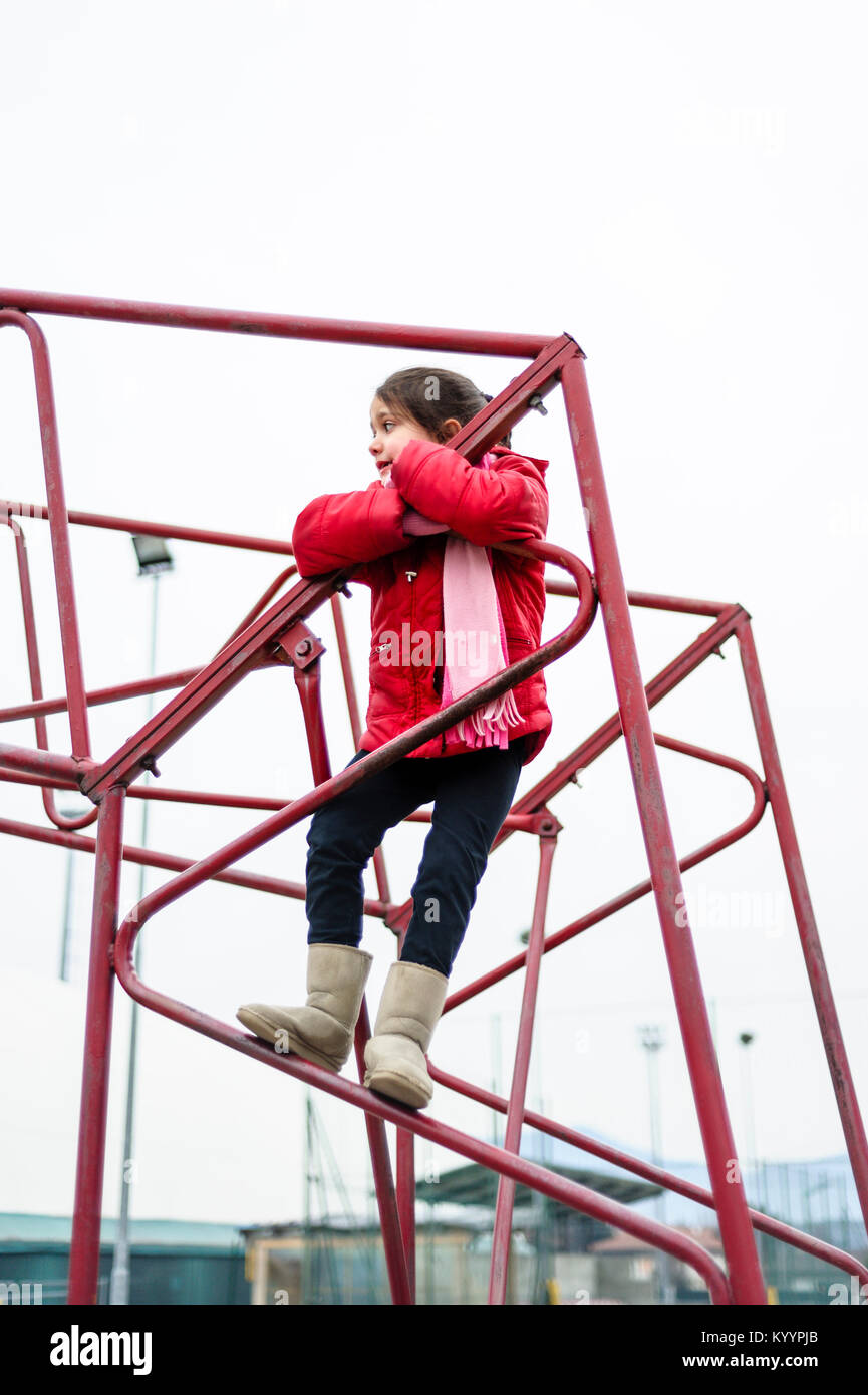 little girl climbs on iron frame of a basketball hoop in an outdoor basketball court Stock Photo
