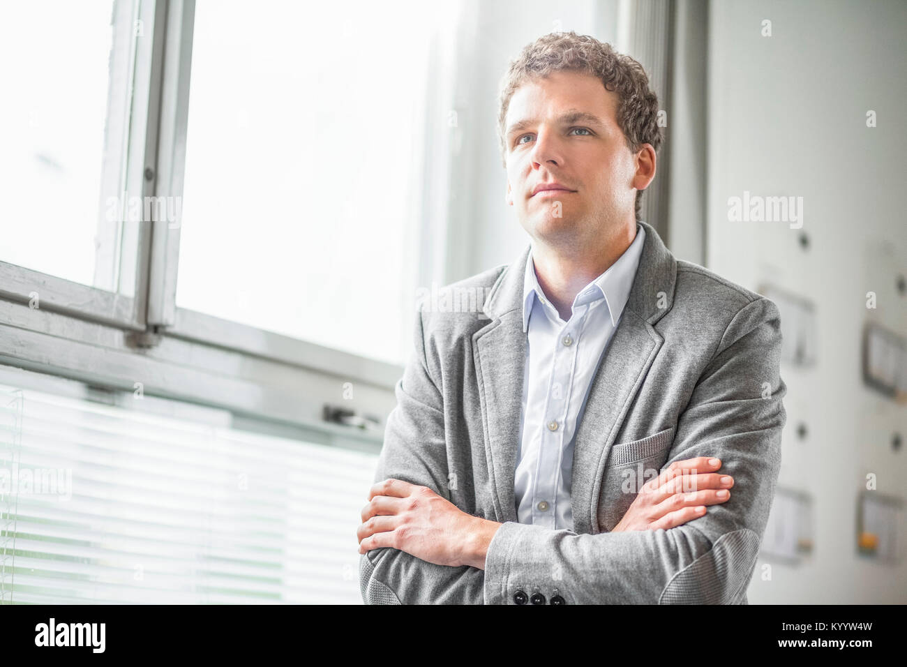 Thoughtful young businessman standing arms crossed in office Stock ...