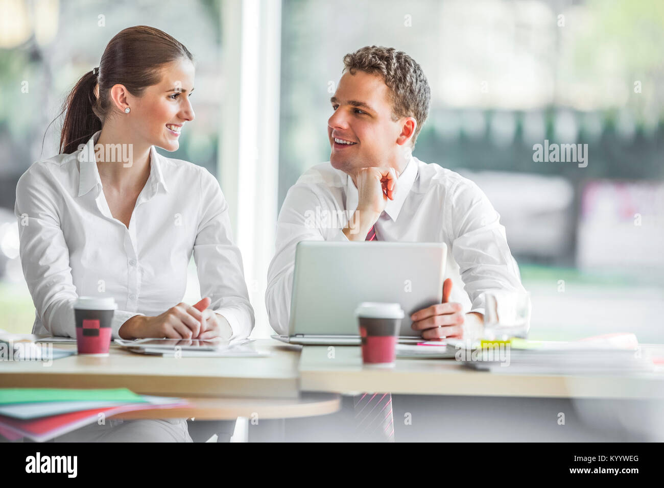 Smiling young businesspeople discussing at office desk Stock Photo - Alamy