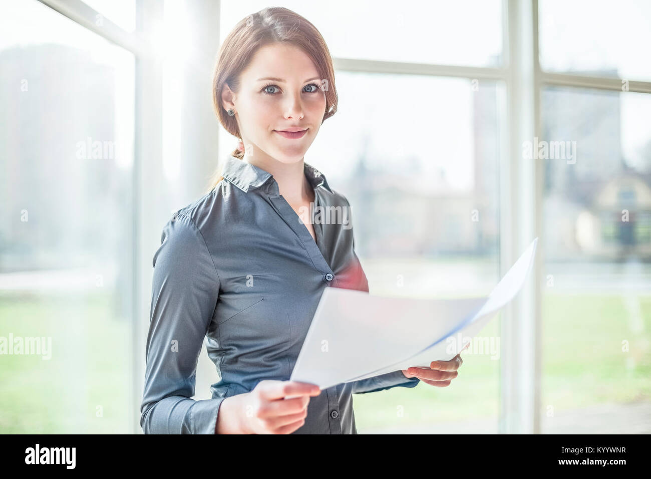 Portrait of beautiful young businesswoman holding documents in office ...