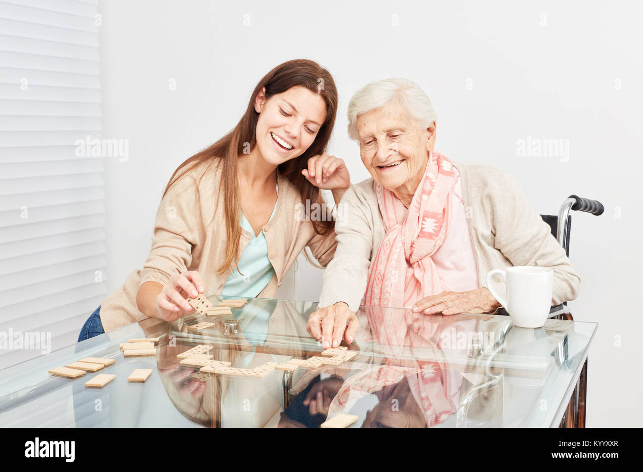 Senior plays with a nursing help together Domino in retirement home Stock Photo