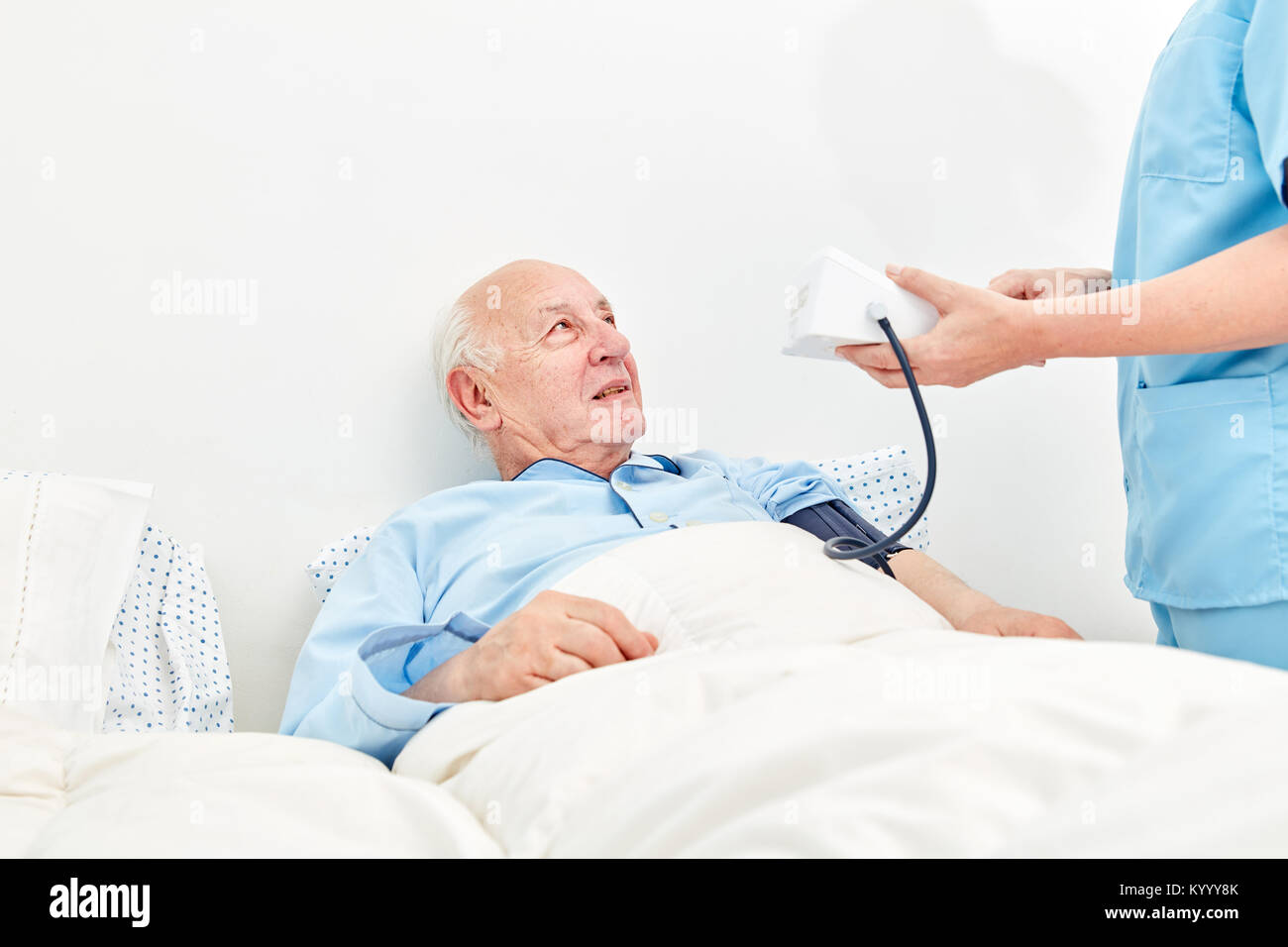 Caregiver measures the blood pressure of an old man as a patient in the hospital Stock Photo
