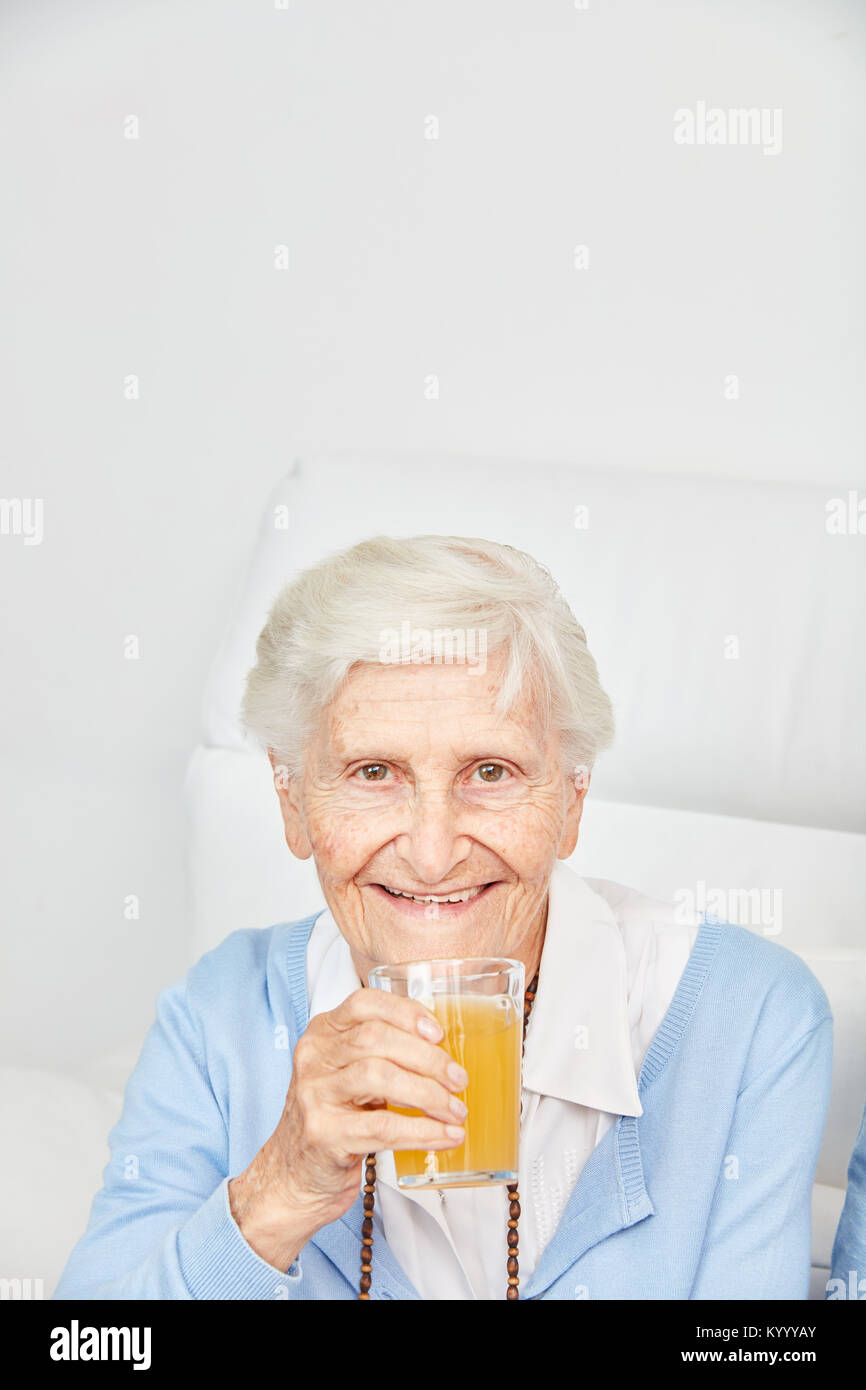 Happy senior citizen drinks a glass with orange juice at home or in retirement home Stock Photo