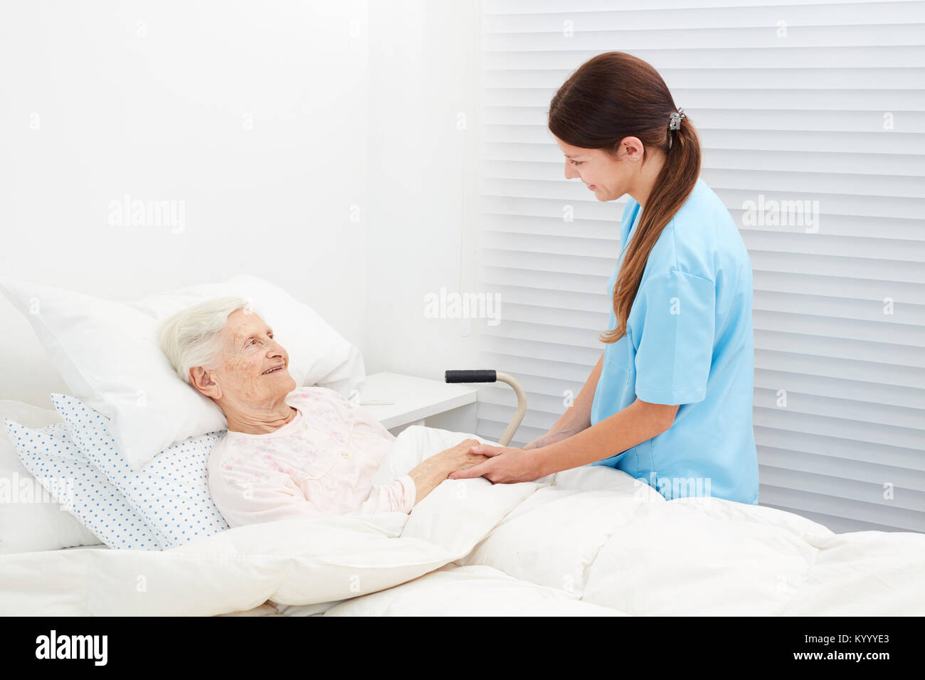 Senior lying in bed in hospice and talking to a caring caregiver Stock Photo