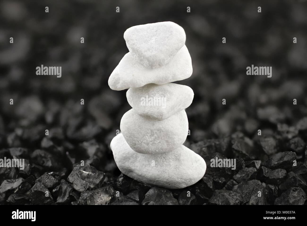 Stacked white pebbles against a black background of grit Stock Photo
