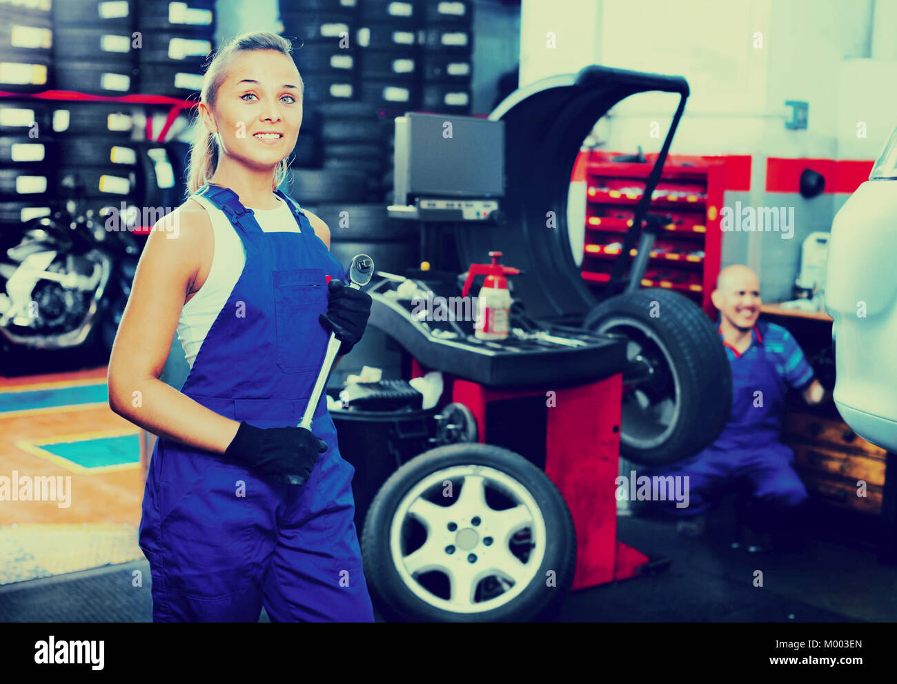 Cheerful smiling efficient mechanic woman working on new tire fitting