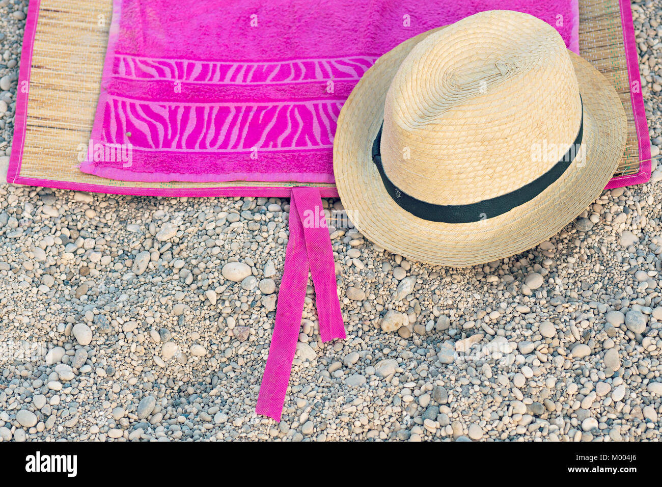 Straw summer hat on a pink towel on a gravel beach Stock Photo