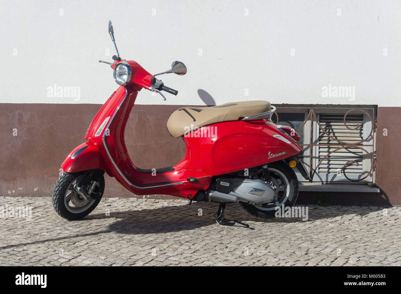 bright red Vespa motor scooter parked on a cobbled street. Stock Photo