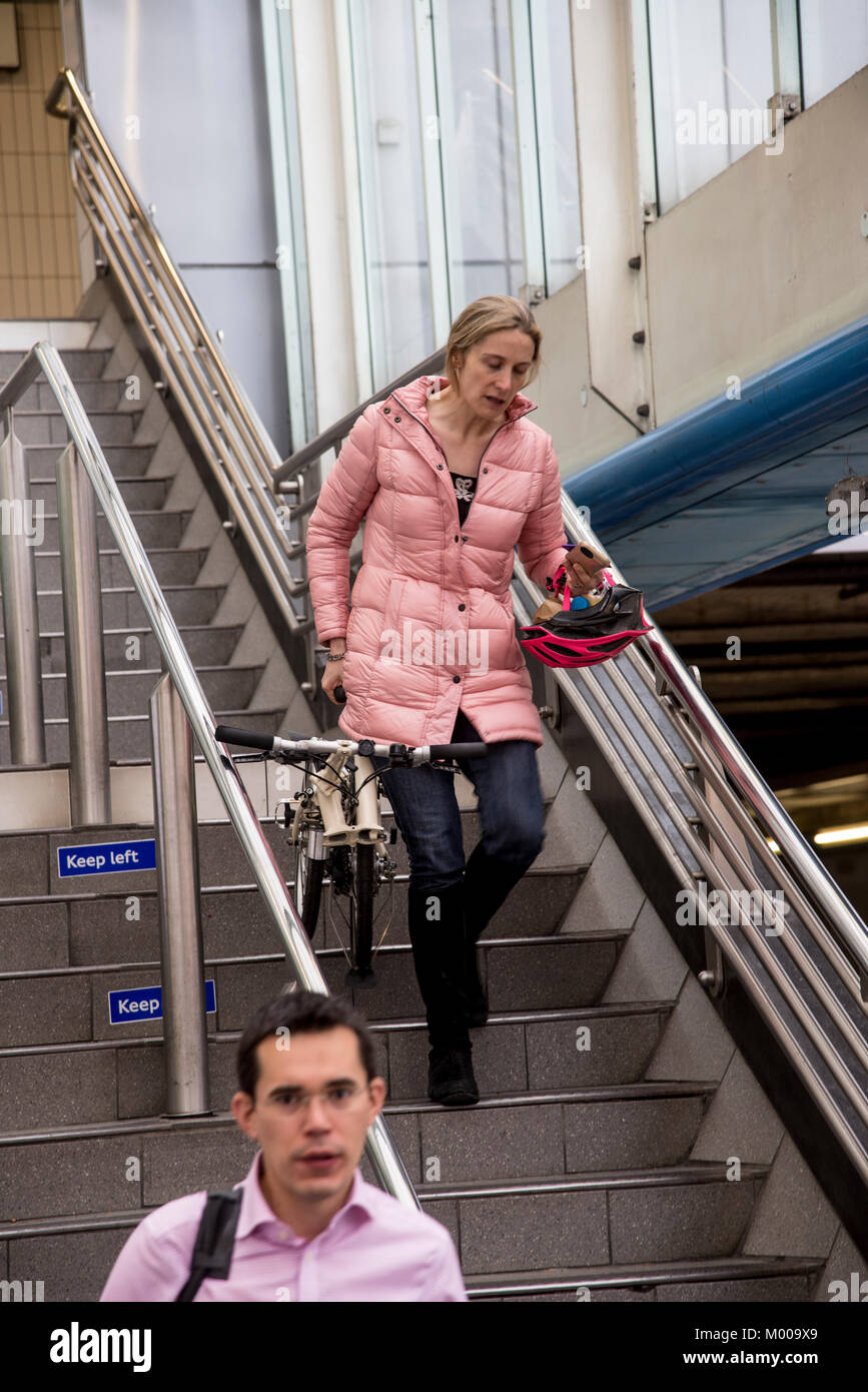 A woman tries to go down the stairs att Hammersmith underground station while carrying a folded bike, London, 2017 Stock Photo