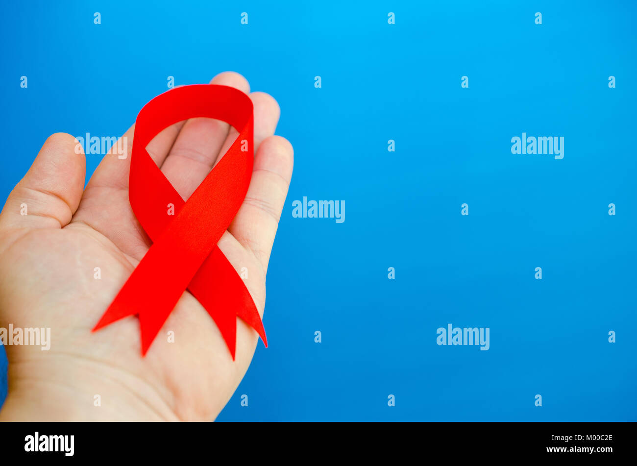 Red folded ribbon in hand on a blue background as a symbol of hemophilia Stock Photo