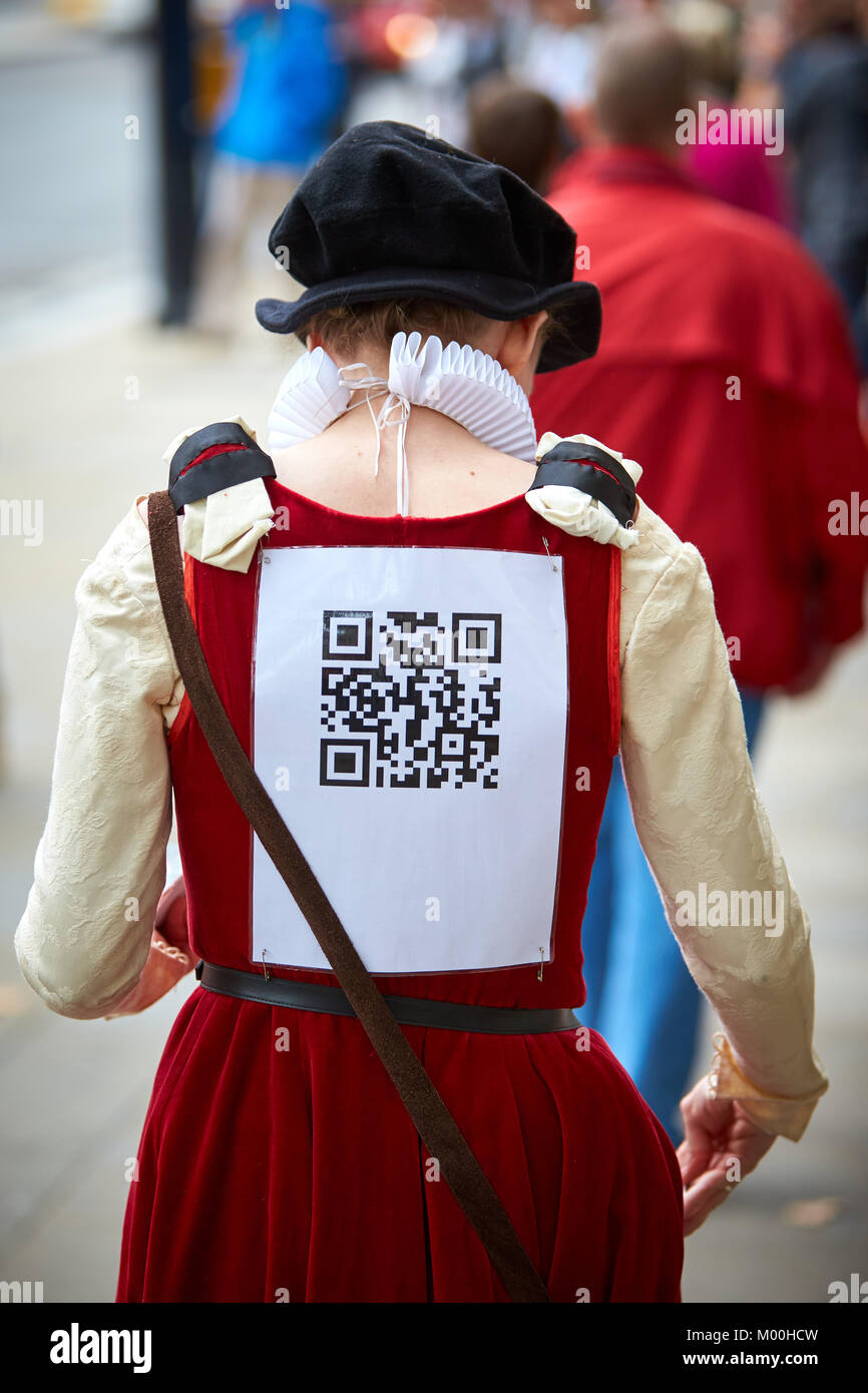 A ticket seller dressed in period costume with a QR code taped to her back in London Stock Photo