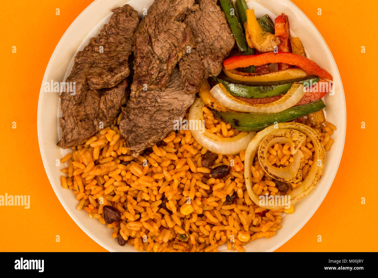 Mexican Style Steak Fajitas With Spicy Rice and Peppers Against An Orange Background Stock Photo