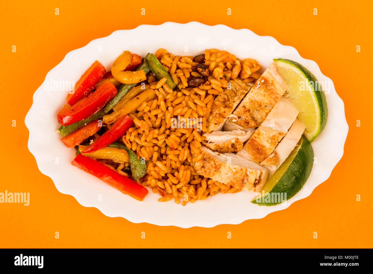 Mexican Style Chicken With Spicy Rice and Fried Peppers Against An Orange Background Stock Photo