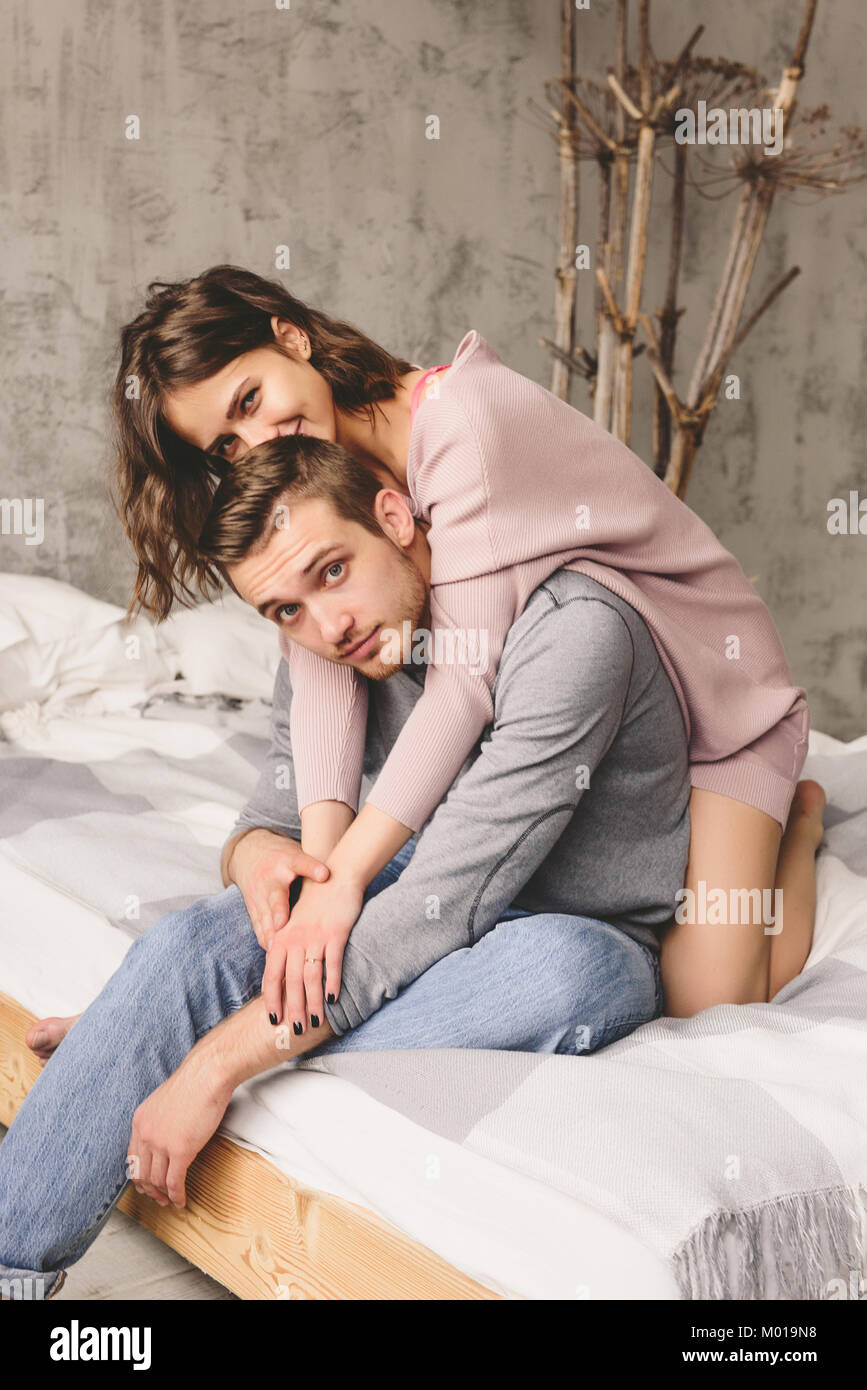 Loving couple. Handsome young hipster with beard and attractive woman resting at home while sitting on bed at home. Stock Photo