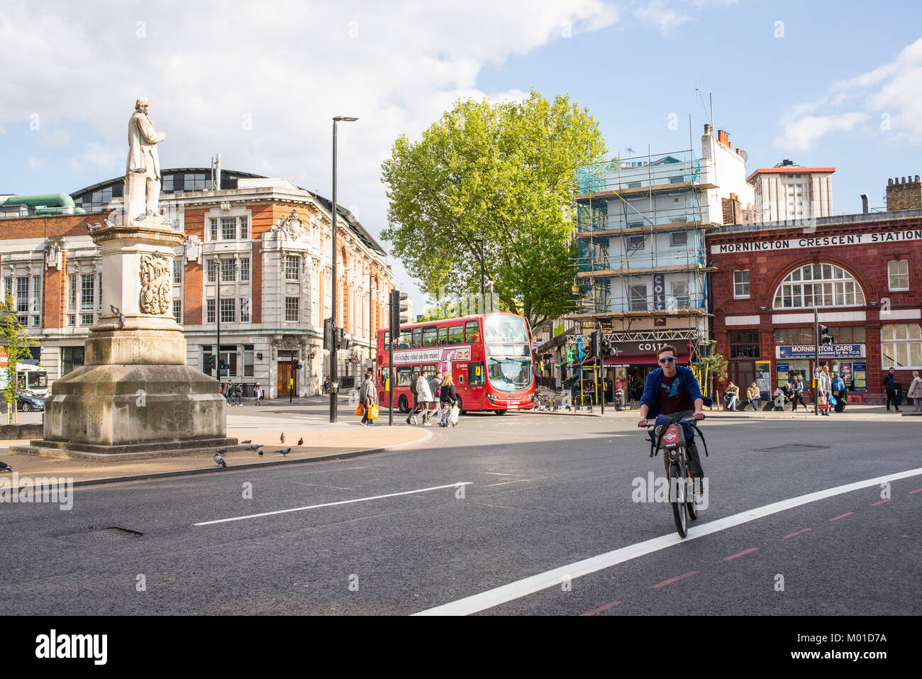 London, UK - April 2017. Cyclist on Santander bike and people walking plus red bus in the background in front of Mornington Crescent Underground Stati Stock Photo