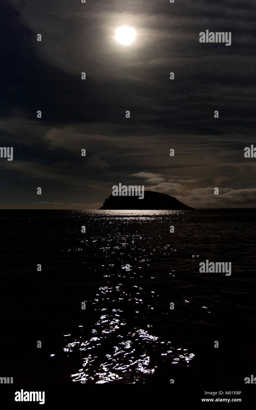 A bright moon over the ocean casts a beautiful, moody reflection off the shiny surface of the water Stock Photo