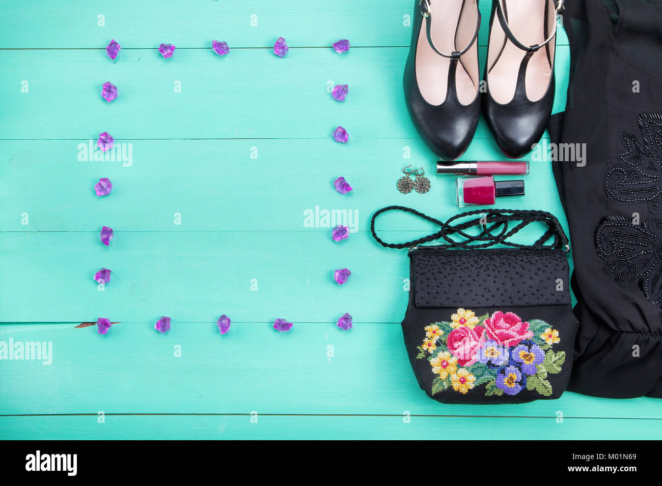 spring clothes, women's clothes - a purple dress, embroidered bag, black heels, earrings, nail polish, lipstick. turquoise wooden background, top view Stock Photo
